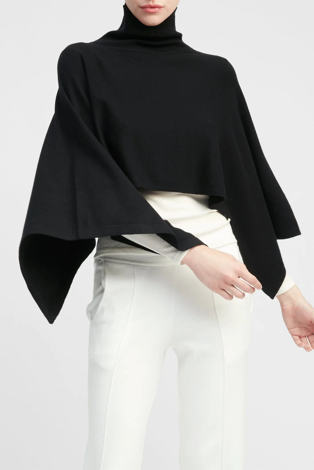 Person wearing a black poncho over a white outfit on a plain background