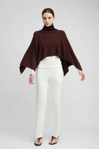 Woman wearing a burgundy poncho and white pants on a gray background