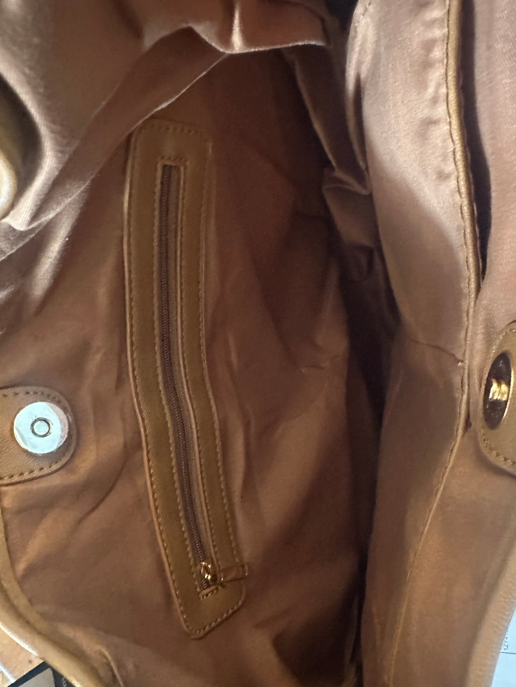 Close-up of a brown leather handbag or interior showing a zippered pocket, snap button closure, and interior pockets.